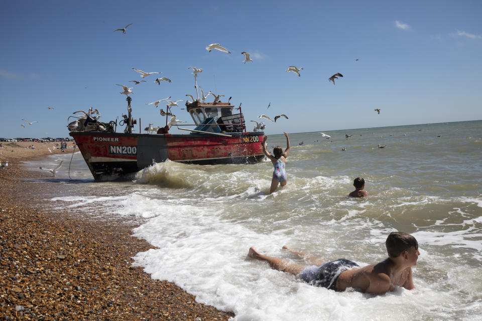 Children play in the sea as a fishing boat returns from an overnight catch in Hastings