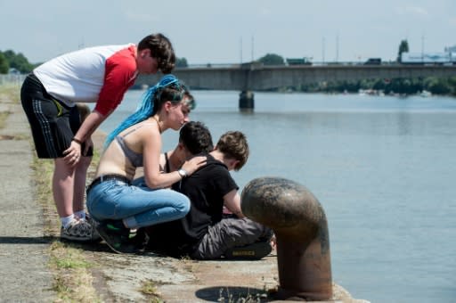Relatives sit on the banks of the Loire river where 24-year-old Steve Canico disappeared after falling in the river following a police intervention at a techno music festival in Nantes