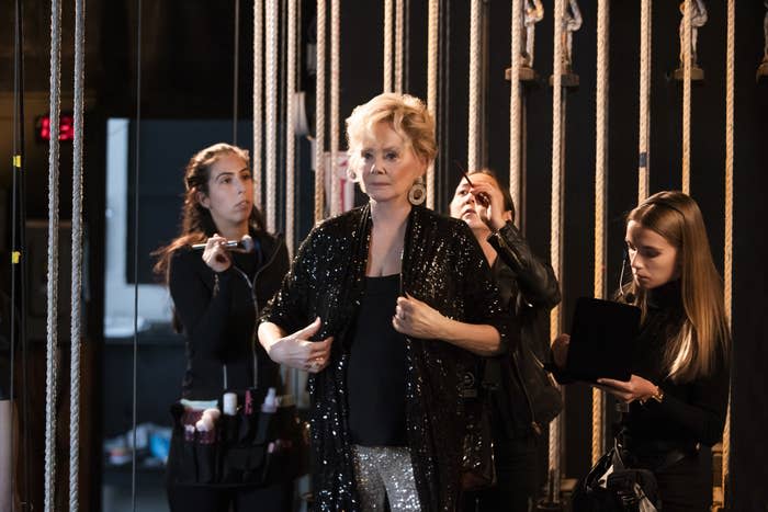 An elderly glamorous woman (Jean Smart) dressed in black prepping herself backstage