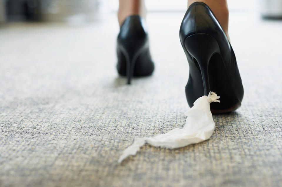 A person in high heels stepping on a piece of tissue on the floor.