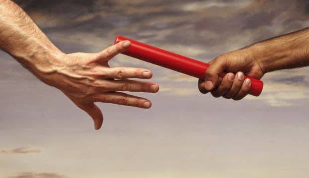 Close-up on the Hand of a Male Athlete Passing a Relay Baton to Another Athlete, With a Dramatic Sky in the Background