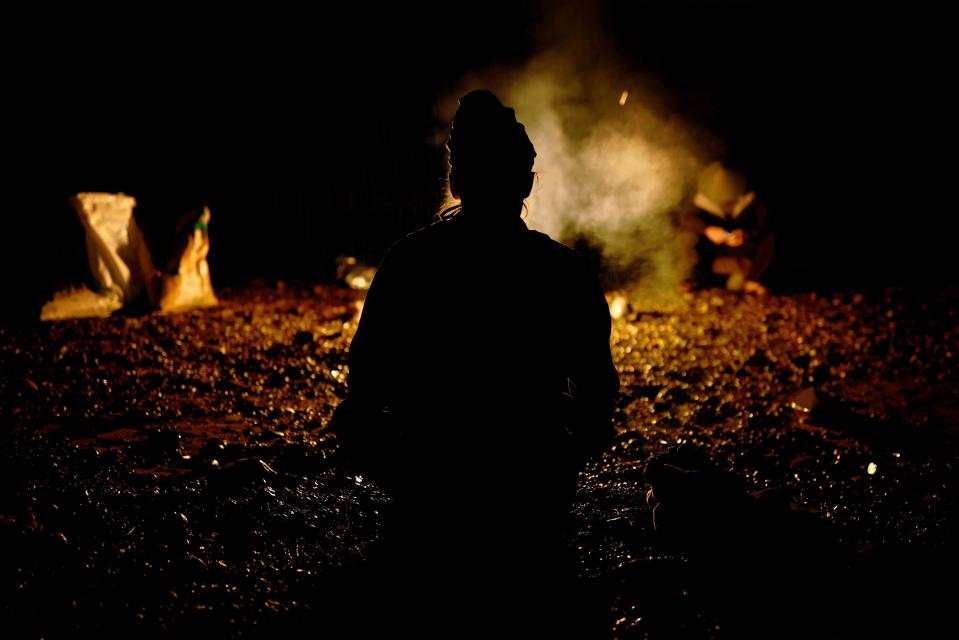 A silhouette of a cormorant fisher kneeling in front of a fire.