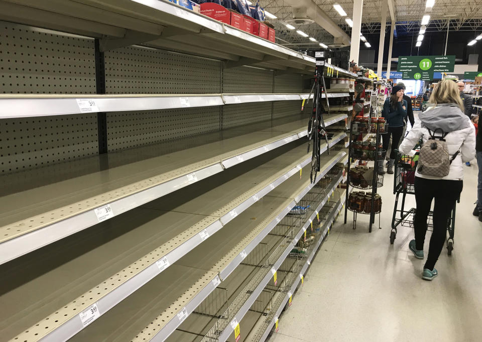 Shoppers walk by near empty shelves at a grocery store in North Vancouver, British Columbia, Saturday, March 14, 2020. (Jonathan Hayward/The Canadian Press via AP)