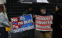 Pro-Brexit campaigners stand under umbrellas with their placards outside the Houses of Parliament in London, Monday, Oct. 21, 2019. The European Commission says the fact that British Prime Minister Boris Johnson did not sign a letter requesting a three-month extension of the Brexit deadline has no impact on whether it is valid and that the European Union is considering the request. (AP Photo/Alastair Grant)