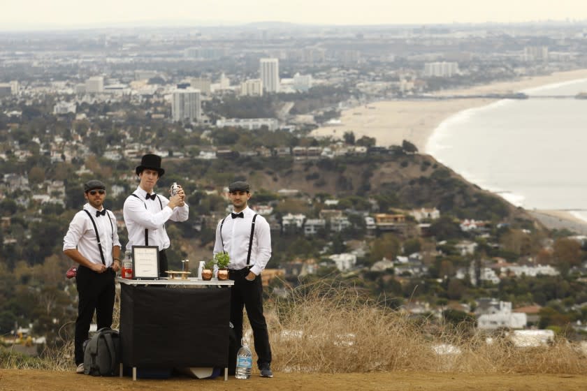 PACIFIC PALISADES, CA - NOVEMBER 30, 2019 - Jack Petros, 28, from left, David Weber, 27, and Dylan Skolnik, 24, members of the Summit Sippers, stand ready to make free drinks for hikers along the Liones Trail in Pacific Palisades on November 30, 2019. Santa Monica Bay and the Santa Monica Pier is viewed in the background. Summit Sippers set up impromptu little bars at random view spots on L.A. hiking trails. They wear bow ties, suspenders and one wears a top hat. They are all avid hikers who enjoy the experience of hiking and than setting up their impromptu watering hole. The drinks are free and they won't even take tips. They are careful not to leave trash behind or block spots where hikers might like to take photos. They try and find picturesque sites along LA's hiking trails. (Genaro Molina / Los Angeles Times)