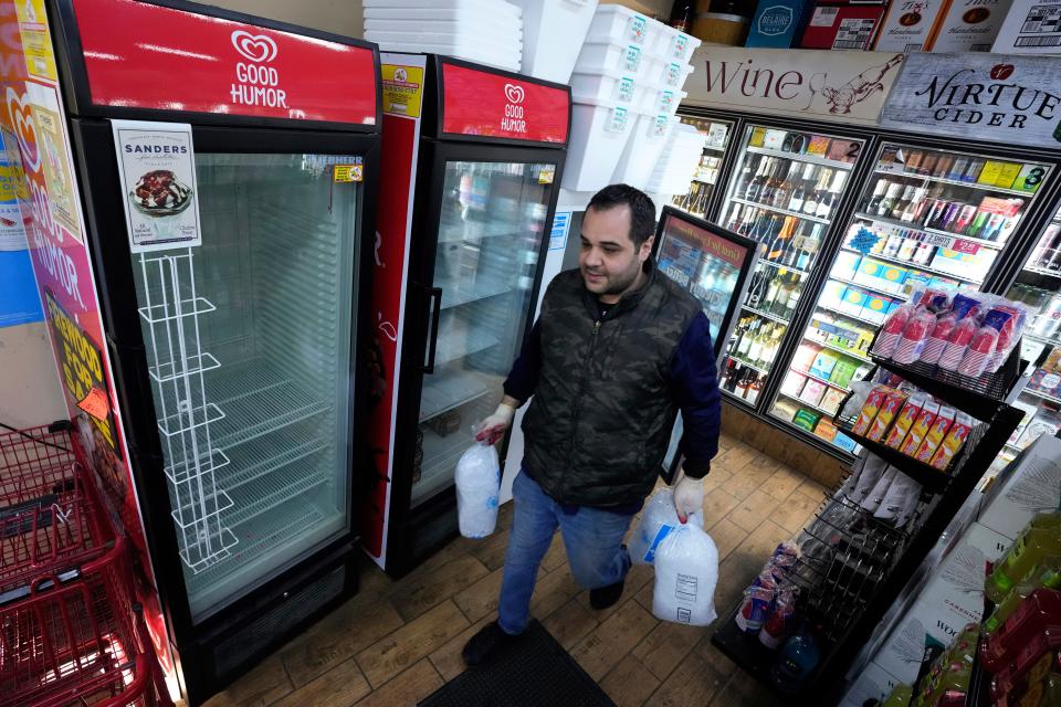 Kevin Savaya, manager at Mr. C's Deli, carries bags of ice past empty coolers in Grosse Pointe Farms, Mich., Friday, Feb. 24, 2023. The business was staying open using a generator. Michigan is shivering through extended power outages caused by one of the worst ice storms in decades.