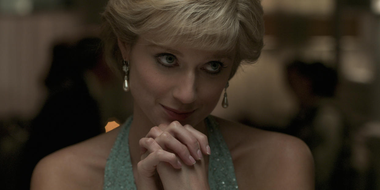 Elizabeth Debicki, as Princess Diana in The Crown, sits at a table with her hands clasped.