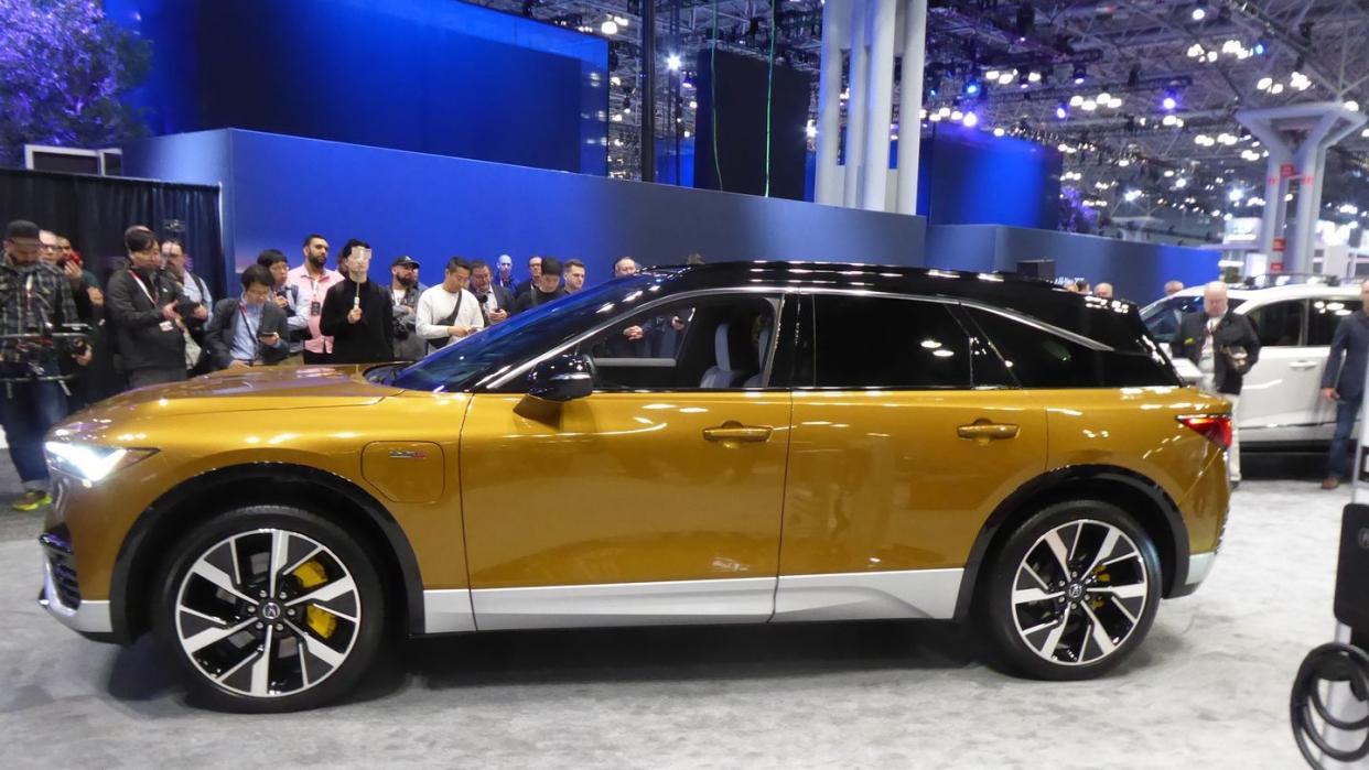 a yellow car parked in a showroom with people standing around 2024 acura zdx type s ev at new york auto show