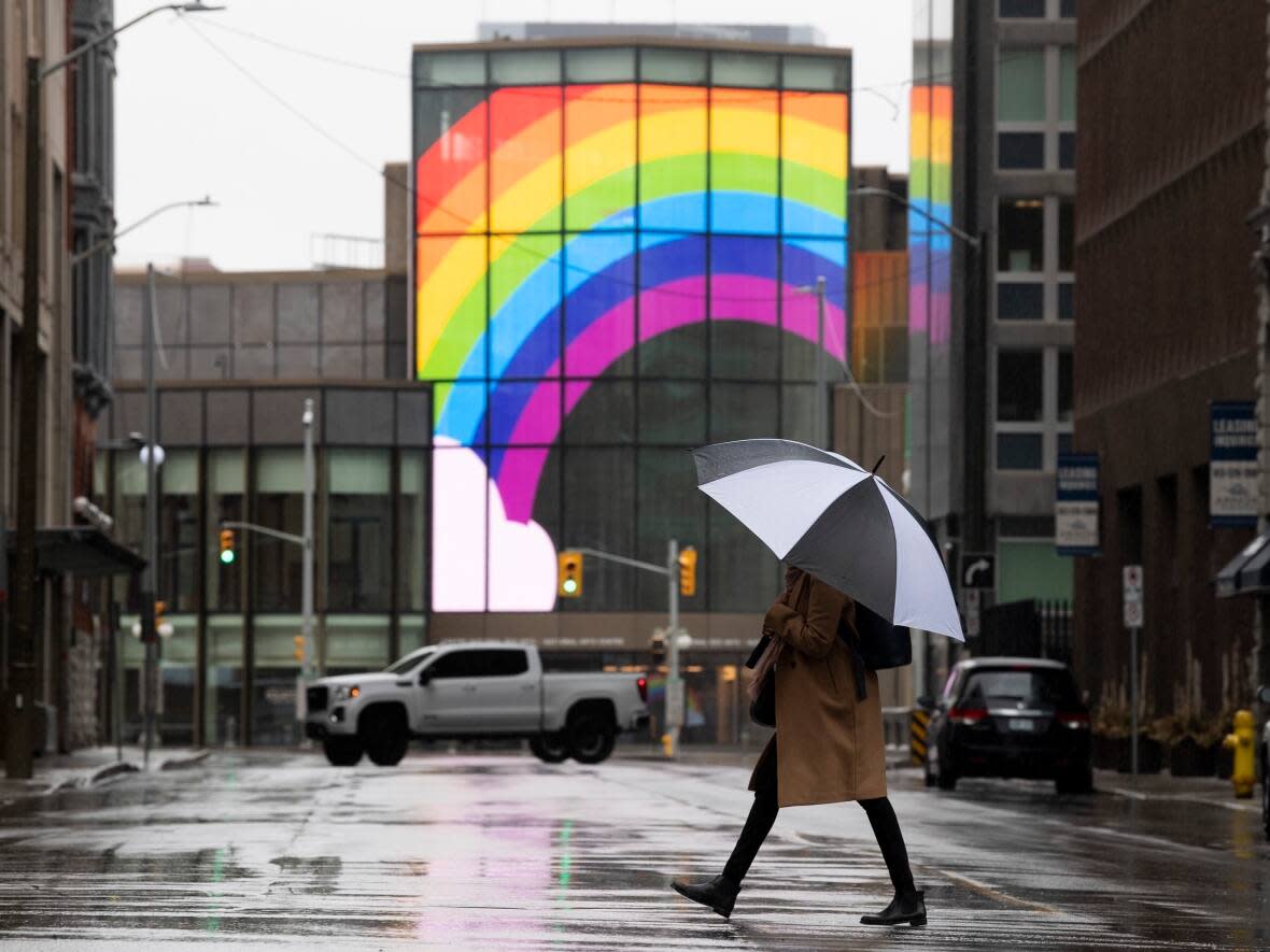 A large rainbow is shown on the National Arts Centre as a woman walks through downtown Ottawa during the COVID-19 pandemic. (Adrian Wyld/The Canadian Press - image credit)