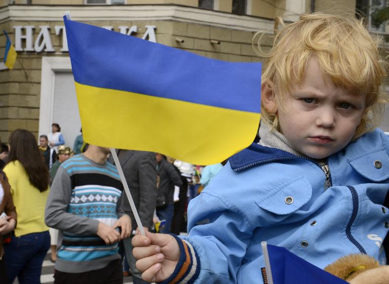 A boy holds a Ukrainian flag as soldiers parade in Mariupol during the celebrations marking the city day on September 20, 2014