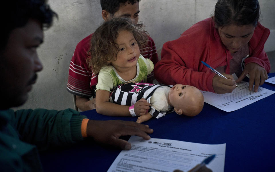 In this Nov. 27, 2018 photo, a child holds her doll as her guardians apply for jobs at a job fair for recently arrived migrants in Tijuana, Mexico. Previously the job fair was only seeing 100 to 130 migrants each day, but the day after the Nov. 25th clash at the border more than 400 had showed up, suggesting that the incident made migrants want to keep their options open.(AP Photo/Ramon Espinosa)