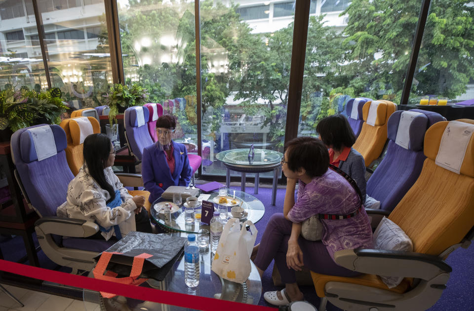 A flight attendant talks to customers after serving meals in a flight-themed restaurant at the Thai Airways head office in Bangkok, Thailand on Oct. 3, 2020. The airline is selling time on its flight simulators to wannabe pilots while its catering division is serving meals in a flight-themed restaurant complete with airline seats and attentive cabin crew. The airline is trying to boost staff morale, polish its image and bring in a few pennies, even as it juggles preparing to resume international flights while devising a business reorganization plan. (AP Photo/Sakchai Lalit)