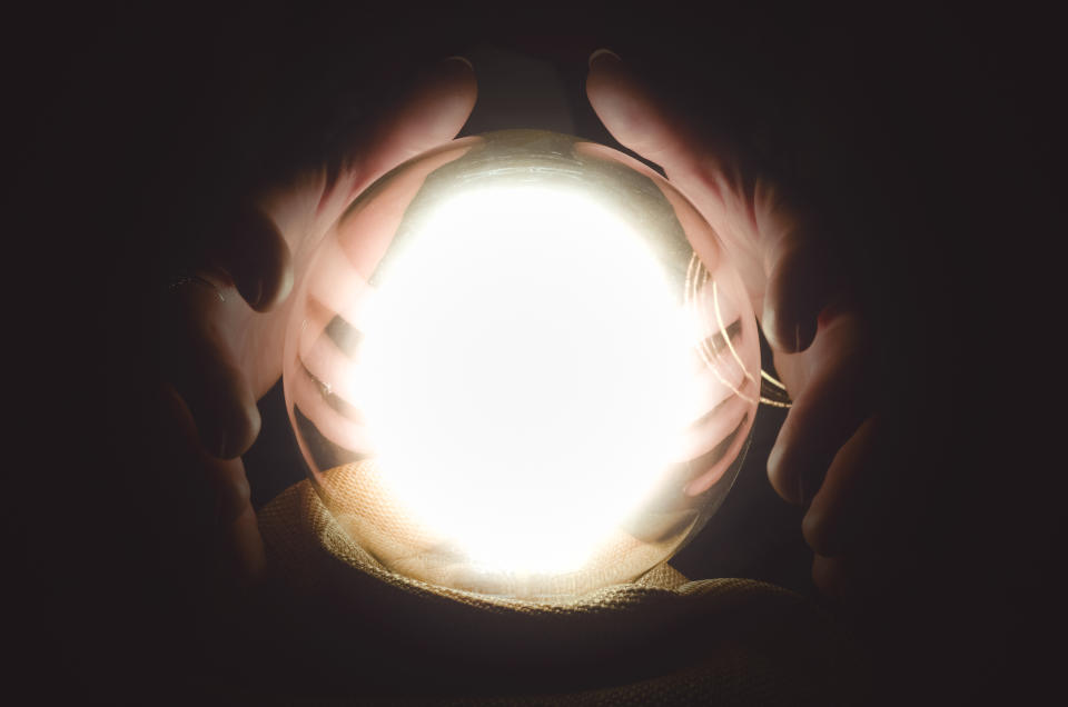 Hands surround a glowing crystal ball.