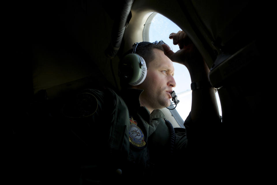 In this Monday, March 24, 2014 photo, a crew member of an Royal Australian Air Force AP-3C Orion patrol plane, looks out of his observation window whilst searching for the missing Malaysia Airlines Flight MH370 over the Indian Ocean. They lean forward as far as they can, occasionally pressing their foreheads against the plane's windows so hard they leave grease marks, staring out at a punishingly unbroken expanse of gray water that seems, at times, to blend into the clouds. Their eyes dart up and down, left and right, looking for something - anything - that could explain the fate of the missing Malaysia Airlines plane. (AP Photo/Richard Wainwright, Pool, File)