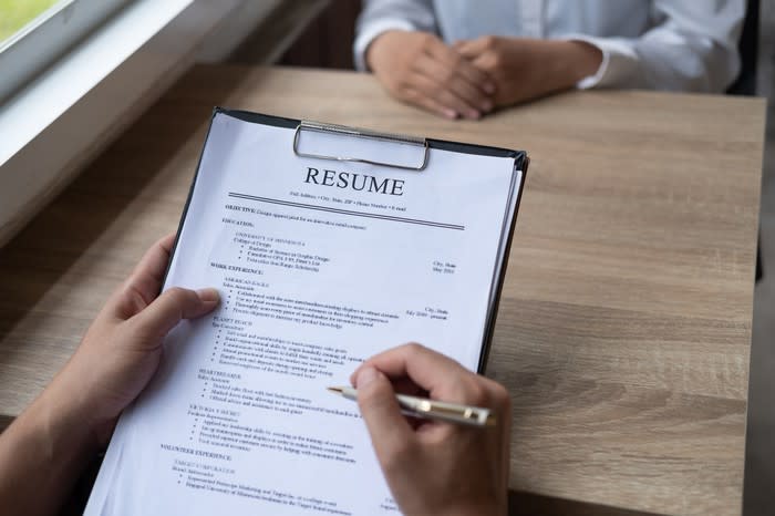 Person holding a pen to a resume on a clipboard while sitting in front of an interviewee.