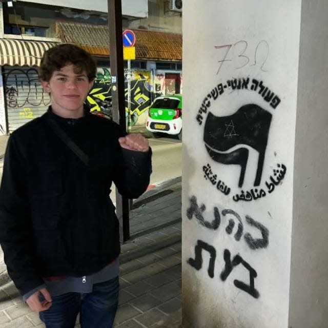 Tal Mitnick stands with a raised fist next to an anti-fascism sign.