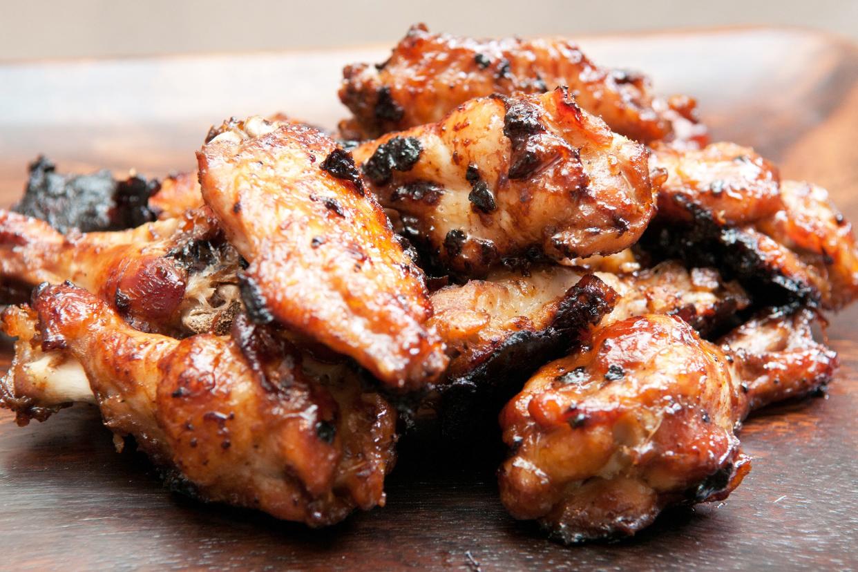 Closeup of many pieces of oven BBQ chicken on a wooden plate with a blurred background