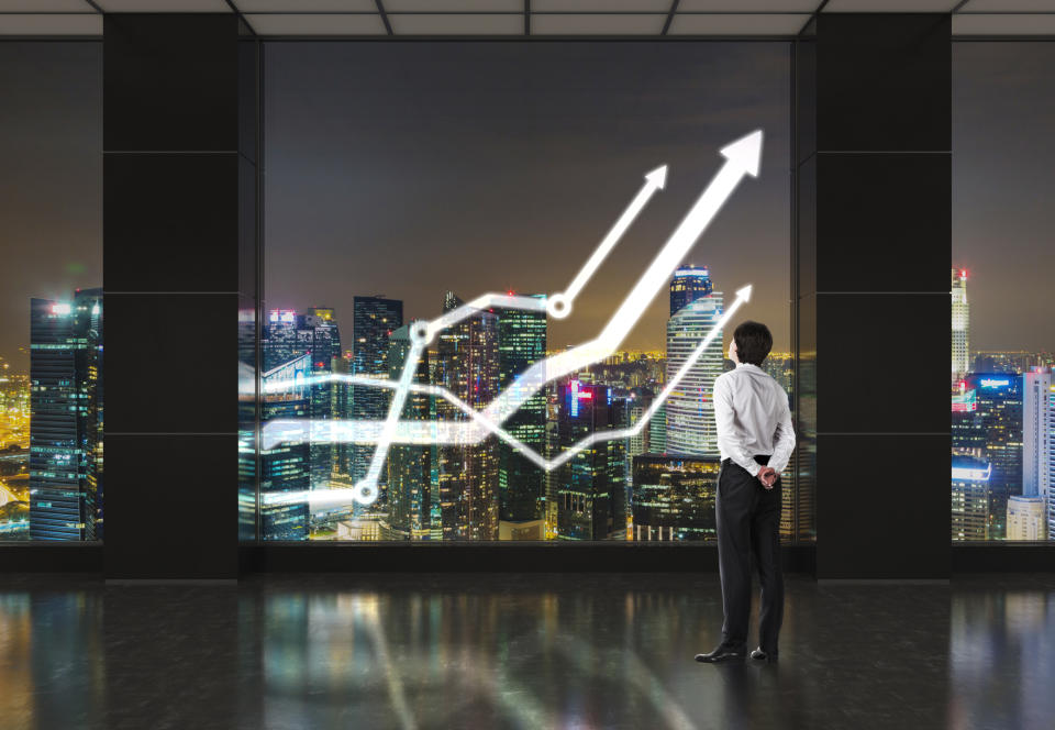 Man looking through window at line charts going up and skyscrapers in background