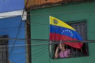 Una mujer se asoma por una ventana donde se puso una bandera nacional de Venezuela para recordar la muerte del fallecido presidente de Venezuela, Hugo Chávez, ocurrida en Caracas, Venezuela, el martes 4 de marzo de 2014. Con motivo del aniversario de Chávez, el presidente Nicolás Maduro ha decretado diez días de conmemoración y que en total suman tres días más de los días de luto oficial que fueron decretados una semana después de su deceso. Chávez murió a los 58 años el 5 de marzo de 2013. Para el miércoles está previsto un desfile militar y una serie de homenajes en el mausoleo donde yacen sus restos y donde Maduro presidirá una ceremonia de salva de cañonazos a las 4:25 de la tarde, que es repetida el 5 de cada mes para recordar el momento exacto de la muerte del líder venezolano. (AP Foto/ Rodrigo Abd)