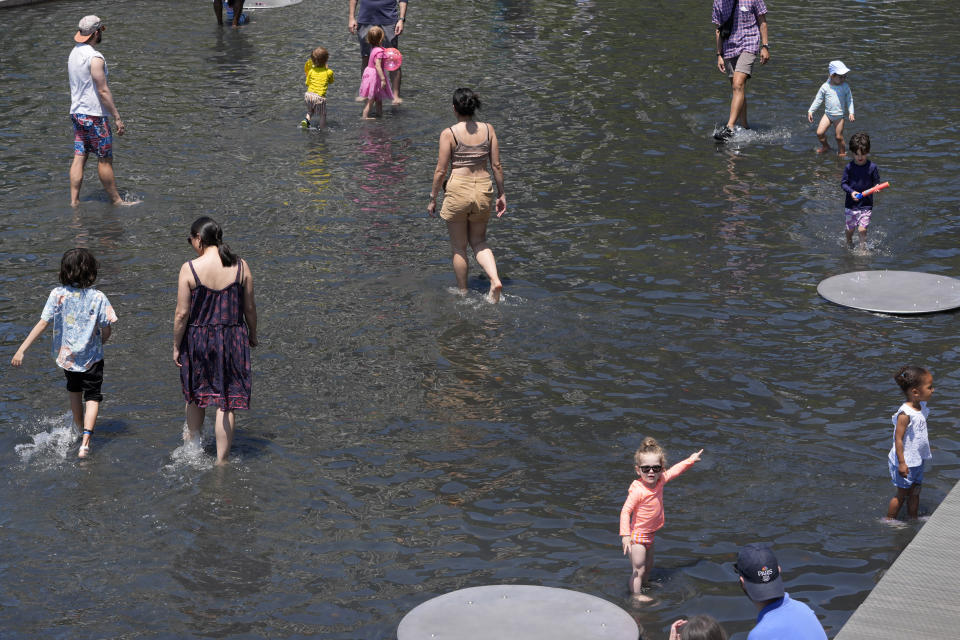 Families wade in ankle deep water at Yards Park Canal Basin, Sunday, June 16, 2024, as temperatures begin to steam up in Washington. The park usually has a waterfall feature which is currently down for maintenance. (AP Photo/Jacquelyn Martin)