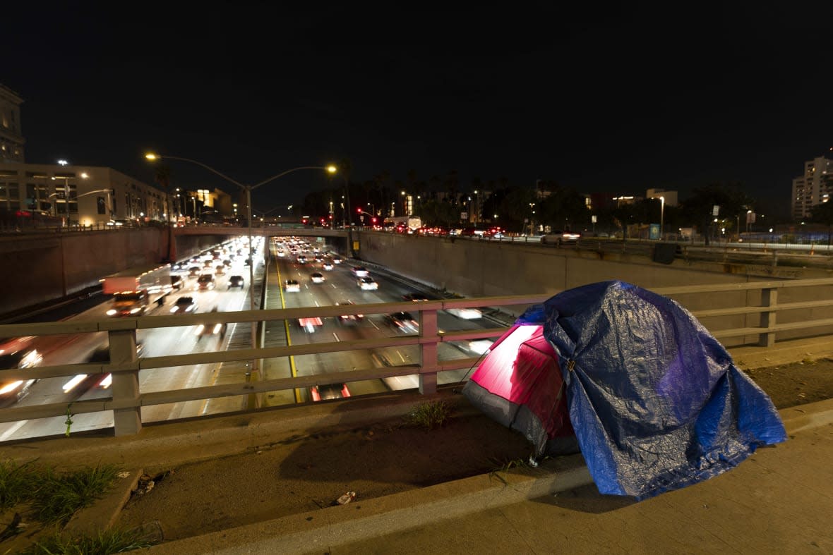 In this photo illuminated by an off-camera flash, a tarp covers a portion of a homeless person’s tent on a bridge overlooking the 101 Freeway in Los Angeles, Thursday, Feb. 2, 2023. (AP Photo/Jae C. Hong, File)