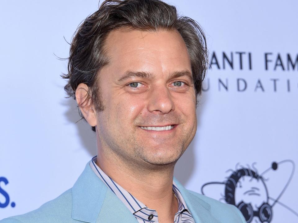 Joshua Jackson poses for photos on the red carpet in a striped shirt and blue suit.