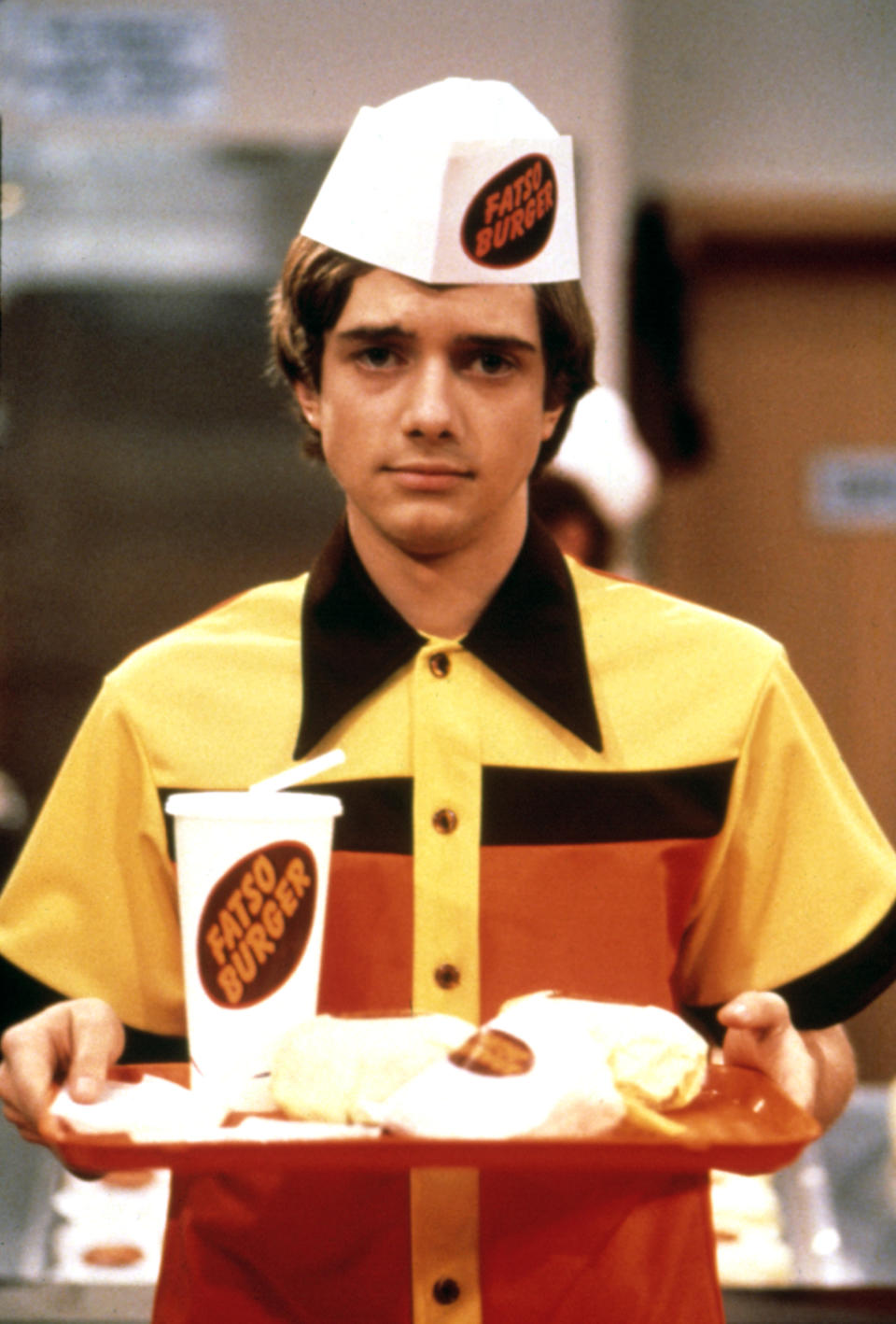 Eric wearing a "Fatso Burger" uniform holds a tray with fast food items