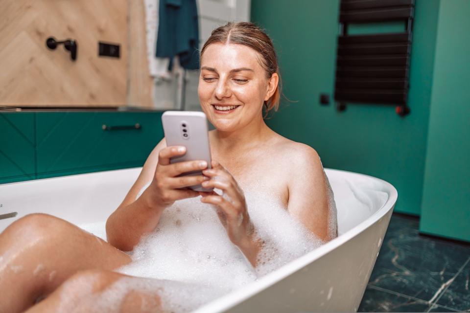 happy pretty caucasian woman using mobile phone while having a bath at home