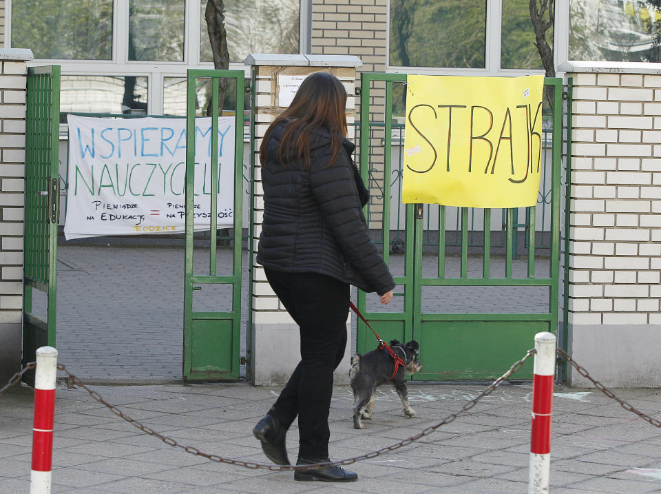 A woman walks by a school where teachers are taking part in nationwide pay strike, with banners declaring the participation in the strike and also parent's support for it, in Warsaw, Poland, Monday, April 15, 2019. The right-wing government says it has money only to grant half of the teachers' demands in a sign that its policy of pre-election spending has reached its limit.(AP Photo/Czarek Sokolowski)