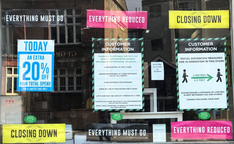 Closing down, reductions and social distancing posters are seen in a closed retail shop window in London