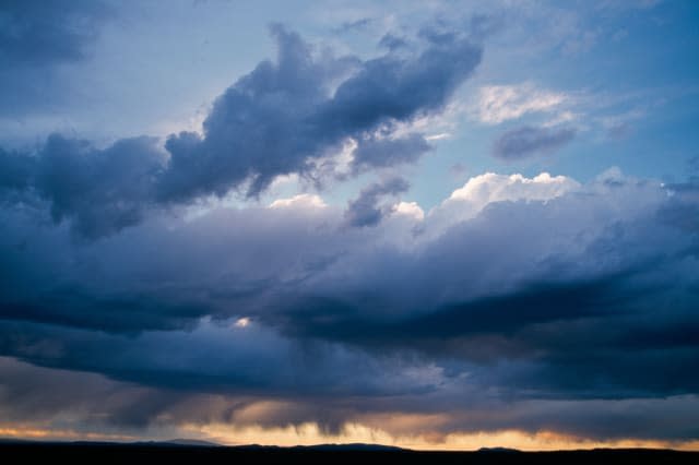 Massive rain clouds at sunset with a skyline of foothills.