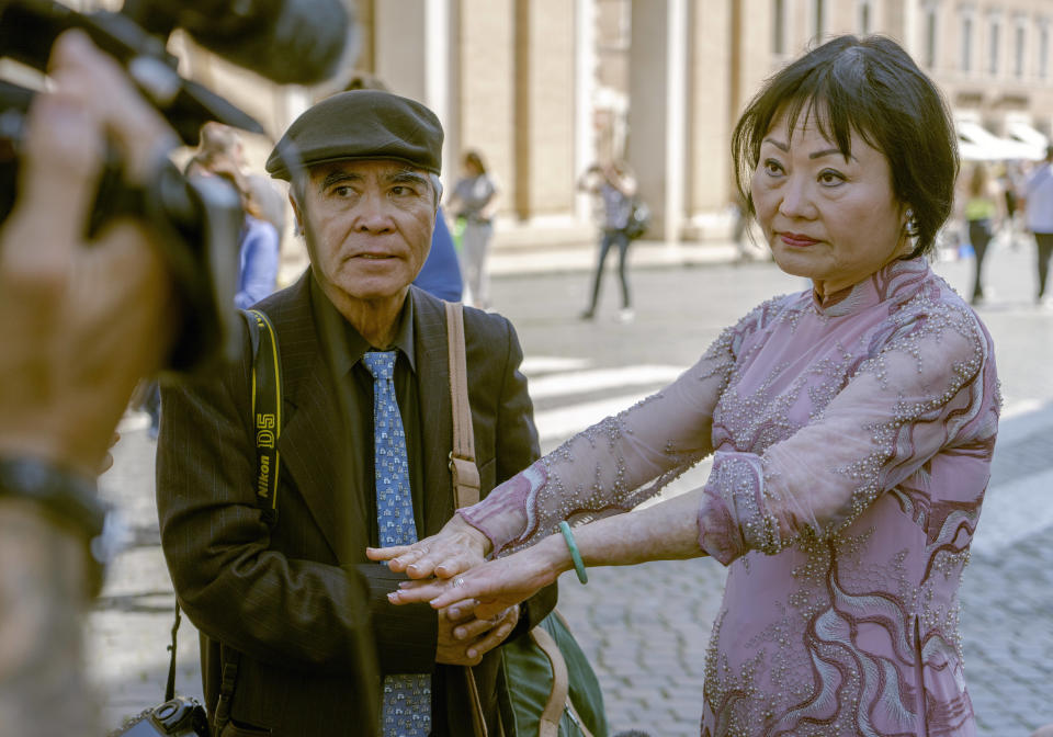 Pulitzer Prize-winning photographer Nick Ut, left, looks at Kim Phuc showing to cameras the scars left by napalm on her body after they met with Pope Francis during the papal weekly general audience in St. Peter's Square at The Vatican, Wednesday, May 11, 2022. Ut and UNESCO Ambassador Kim Phuc are in Italy to promote the photo exhibition "From Hell to Hollywood" resuming Ut's 51 years of work at the Associated Press, including the 1973 Pulitzer-winning photo of Kim Phuc fleeing her village after it was accidentally hit by napalm bombs dropped by South Vietnamese forces. (AP Photo/Domenico Stinellis)