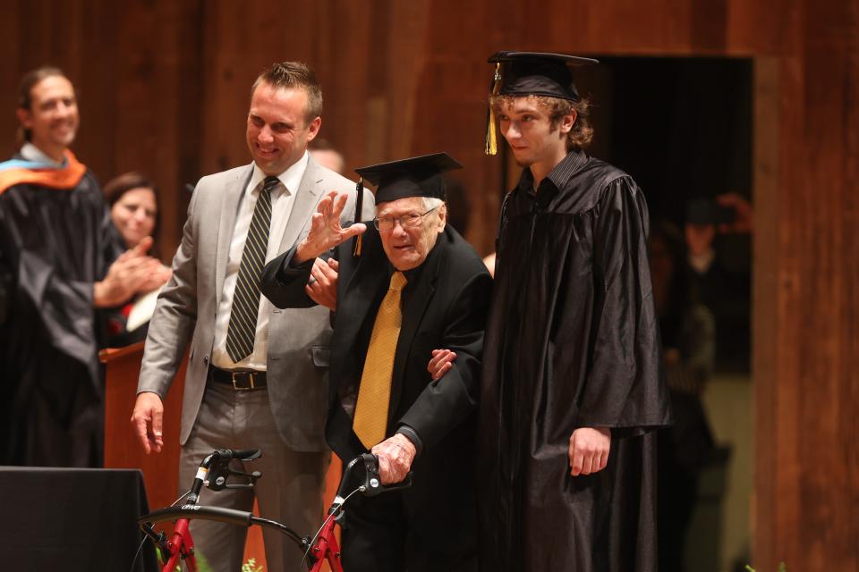 Graduate Libert Bozzelli, 97, gets an escort from family members — Brent Honey, left, who is Bozzelli's grandson and a Cuyahoga Falls teacher, along with Dominick Czetli, who is Bozzelli's great-grandson and a graduating senior — as his name is called at the 2022 Cuyahoga Falls High School commencement ceremony.