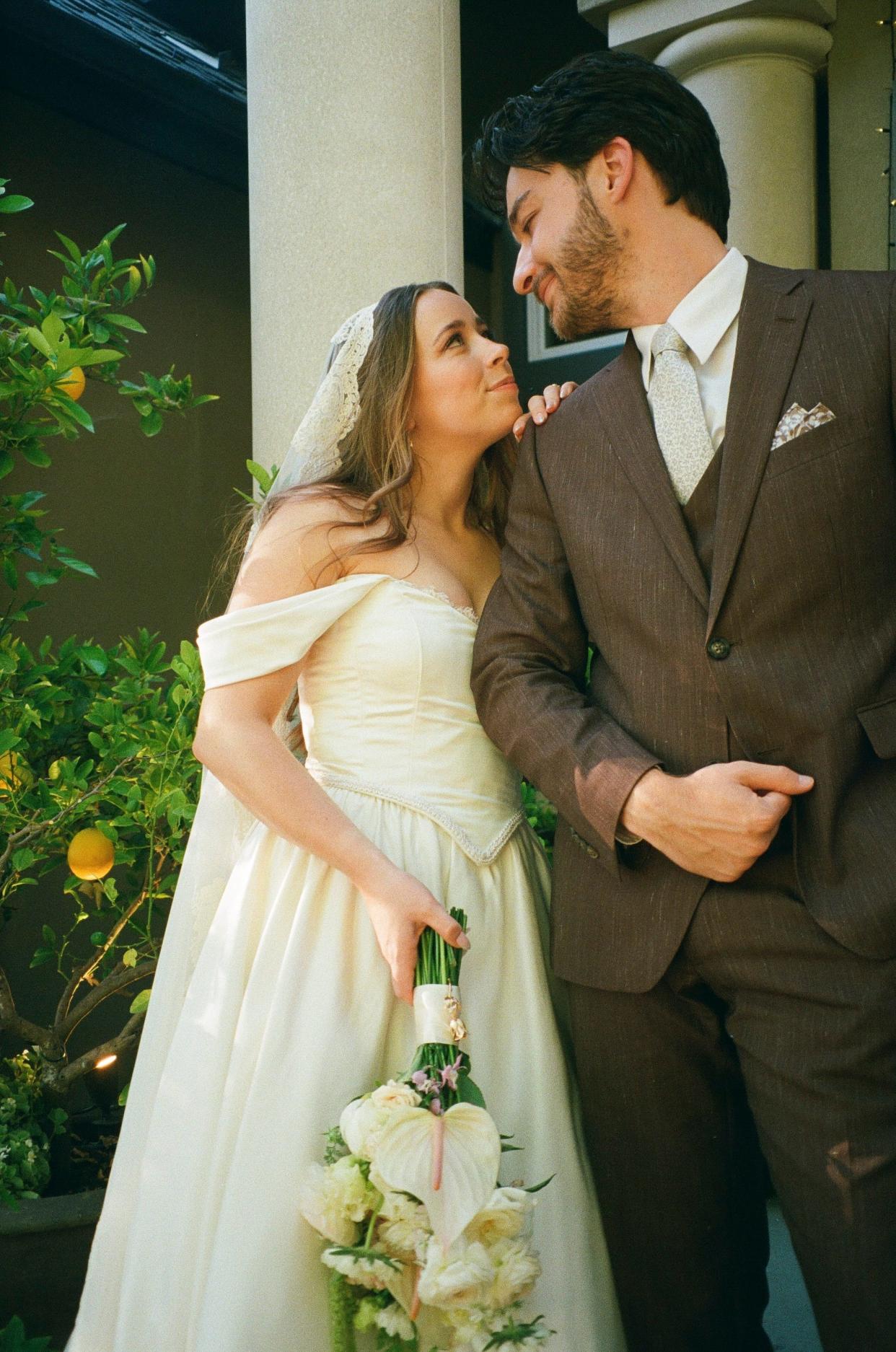 A bride wearing a lace veil leans on her groom's shoulder.