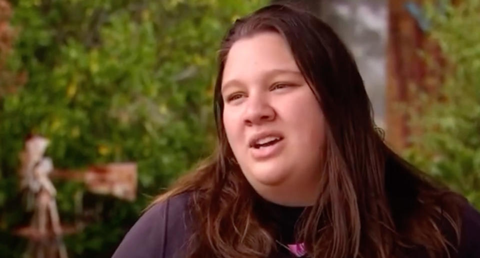 Kaitlyn Bailey speaking to the camera with her long brown hair out and black jumper on. 