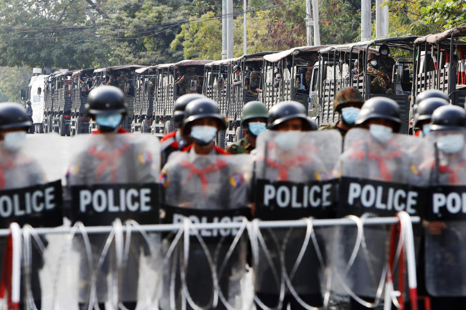 FILE - In this Friday, Feb. 19, 2021 file photo, military trucks with soldiers inside are parked behind police standing guard behind a road barricade in Mandalay, Myanmar. Ever since the military seized control of the country in February, the conflict in Myanmar has become increasingly bloody. Security forces have killed more than 700 people, including a boy as young as 9. (AP Photo)