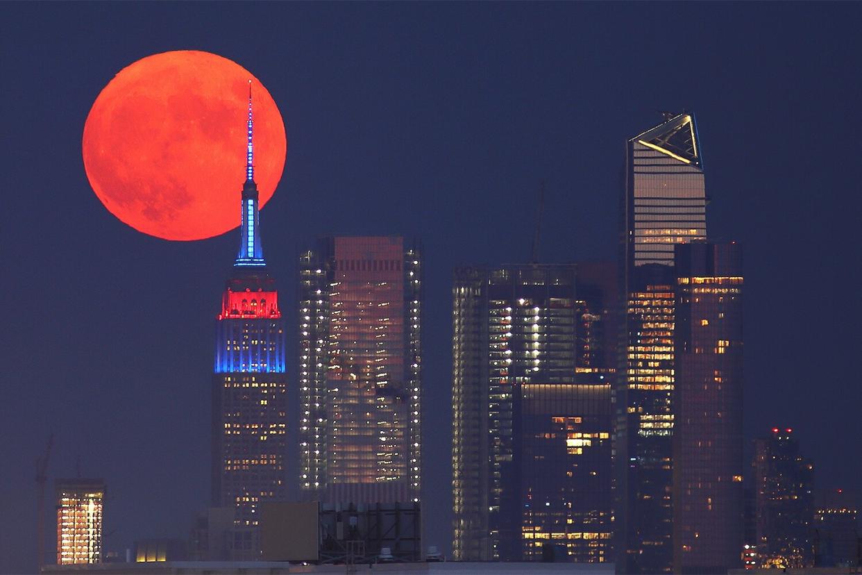 The full Buck Moon or Thunder Moon passes behind Hudson Yards and the Empire State Building lit in the flag colors of countries competing in the Tokyo Olympics as it rises in New York City on July 23, 2021 as seen from Lyndhurst, New Jersey.