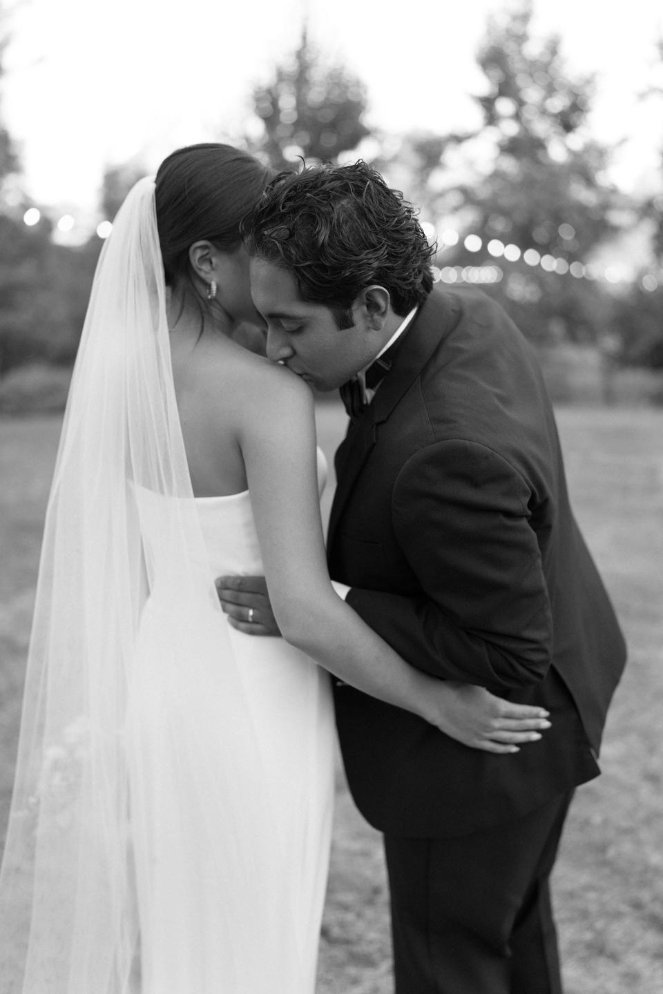 A black and white shot of a groom kissing his bride's shoulder.