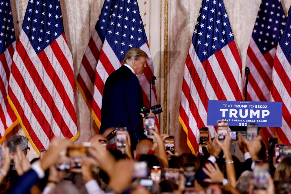 Donald Trump takes the microphone against a backdrop of U.S. flags, as audience members hold their cellphones up to capture the moment. One banner in the crowd says: Trump Make America Great Again! 2024.