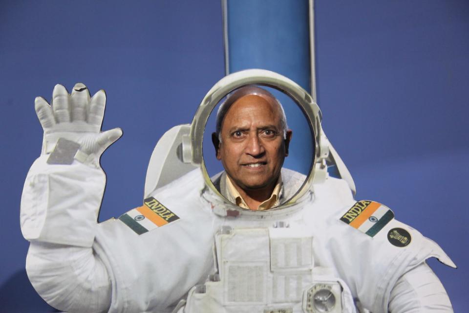 man poses in white waving astronaut uniform with india flag patches on each shoulder