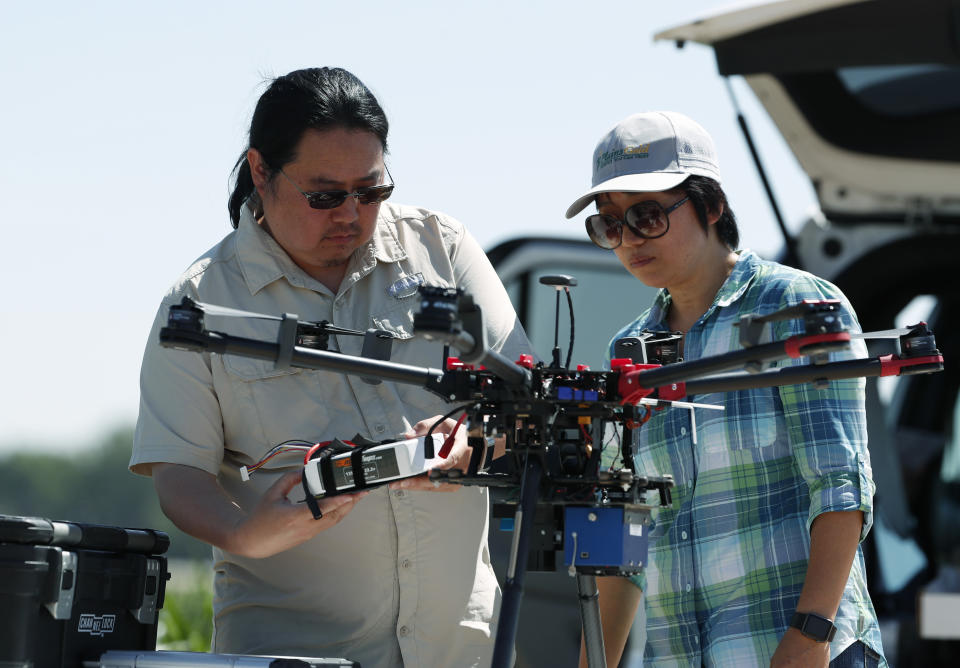 In this Thursday, July 11, 2019, photograph, United States Department of Agriculture engineering technician Kevin Yemoto, left, loads a camera into a drone as Huihui Zhang looks on at a research farm northeast of Greeley, Colo. Researchers are using drones carrying imaging cameras over the fields in conjunction with stationary sensors connected to the internet to chart the growth of crops in an effort to integrate new technology into the age-old skill of farming. (AP Photo/David Zalubowski)