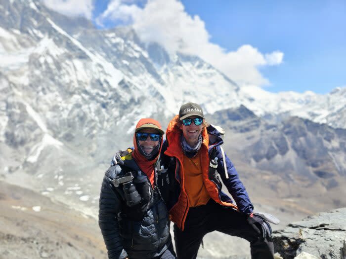 The climbers smile, shoulder to shoulder, with high mountains behind them.