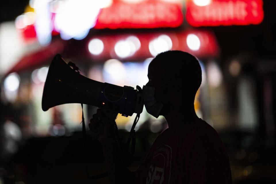 FILE - In this Saturday, July 18, 2020, file photo, Elyas Sow uses a megaphone to speak to people as he and others from Street Corner Resources "Occupy the Corner" of potential areas of conflict and gun violence, in the Harlem neighborhood of New York. A rise in gun violence in cities across the U.S. is testing the limits of anti-violence groups that have been calling for more government funding for decades. President Joe Biden acknowledged earlier this year that community anti-violence programs have been woefully underfunded and has proposed $5 billion in new aid for them. (AP Photo/Frank Franklin II, File)