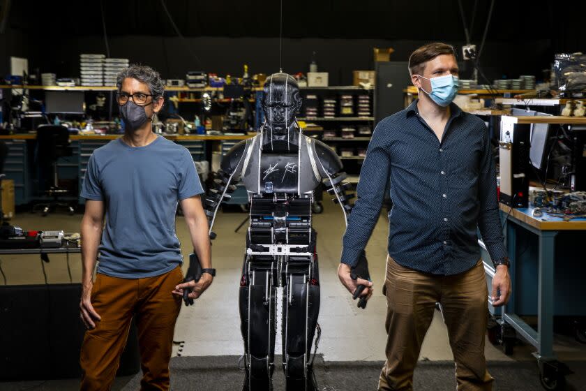 Glendale, CA - June 21: Tony Dohi, Research & Development Imagineer Principal, with Walt Disney Imagineering, left and Morgan Pope, Research Scientist, Robotics, with Walt Disney Imagineering Research & Development, are photographed with an early MkI prototype of their Stuntronics robot, in their lab at Walt Disney Imagineering Research & Development Lab, in Glendale, CA, Monday, June 21, 2021. The prototype, an advanced robotics figure capable of flying through the air and preforming acrobatic feats, was utlized in the new Spider-Man stunt show on the Avengers Campus at Disney California Adventure Park, which opened earlier this month. On the chest of the prototype, are signatures of actor Tom Holland, who portrays Spider-Man in the current films, as well as voicing the new ride and Kevin Feige, president of Marvel Studios and the primary creator and producer of the Marvel Cinematic Universe franchise since 2007. (Jay L. Clendenin / Los Angeles Times)