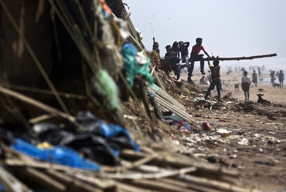 Boys play on a fallen tree trunk amidst the debris of damaged houses belonging to fishermen after Cyclone Phailin hit Puri