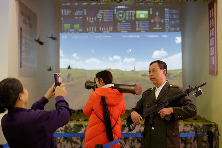 Visitors pose for photos with models of weapons at a military simulator area during an exhibition displaying China's achievements for the past five years, as a part of the celebrations of the upcoming 19th National Congress of the Communist Party of China (CPC) at Beijing Exhibition Centre in Beijing, China October 10, 2017. REUTERS/Jason Lee