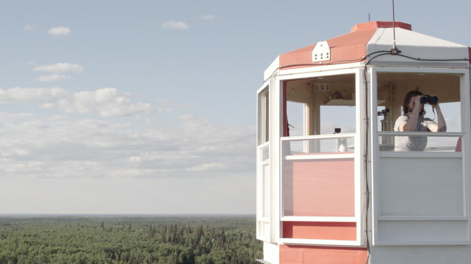 Kimberly Jackson in fire tower lookout, gazing through binoculars spotting smoke in the documentary Fire Tower

