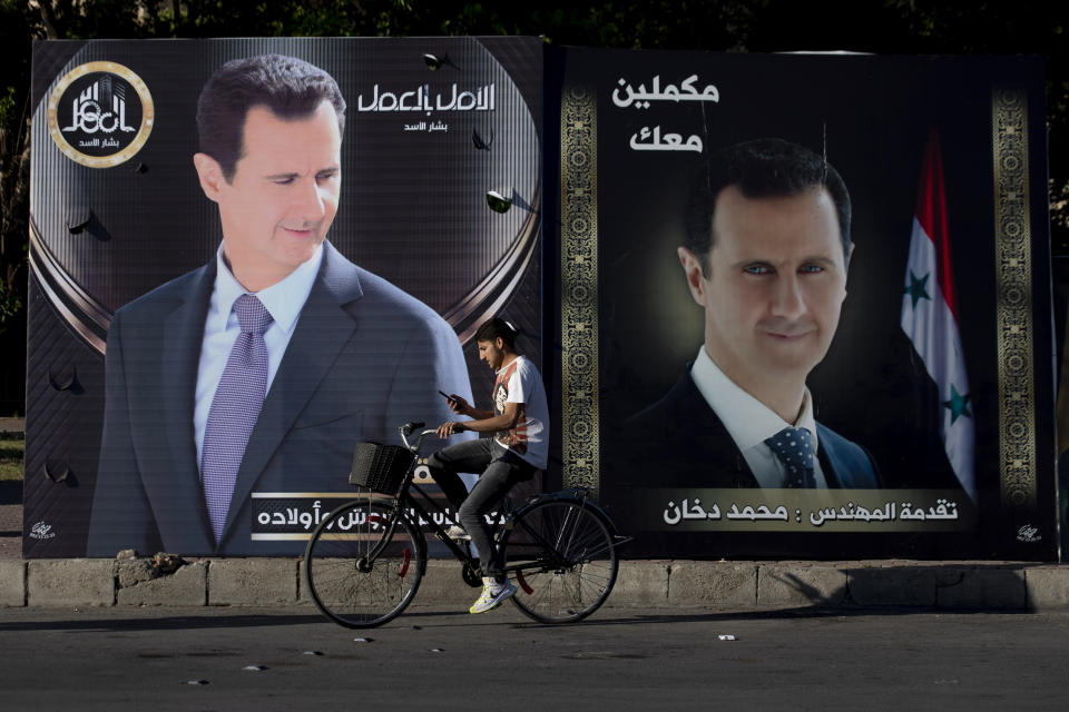 A Syrian man checks his mobile phone as he rides his bicycle past campaign posters of President Bashar Assad for the upcoming presidential election that adorn a street in the Syrian capital Damascus, Sunday, May 23, 2021. The presidential elections in the war-ravaged country will be held May 26. Arabic on the right top reads, "We are continuing with you." (AP Photo/Hassan Ammar)