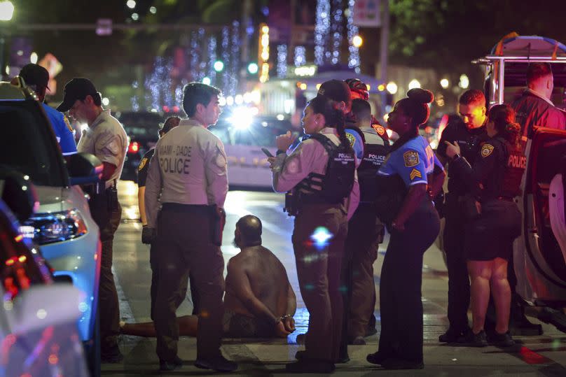 A man sits on the ground handcuffed after witnesses say he appeared to be brandishing a knife in Miami Beach last March