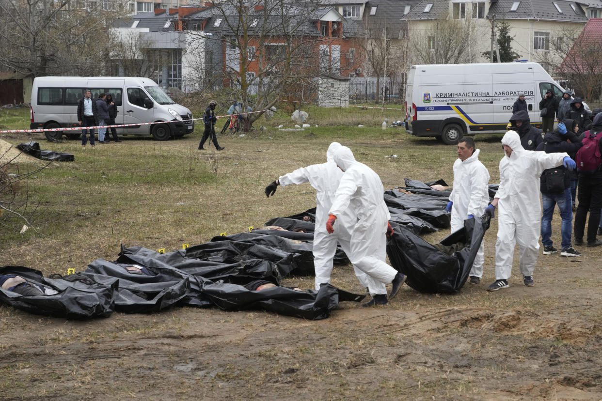 FILE - Men wearing protective gear carry a dead body during the exhumation of killed civilians in Bucha, outskirts of Kyiv, Ukraine, Friday, April 8, 2022.  / Credit: Efrem Lukatsky / AP